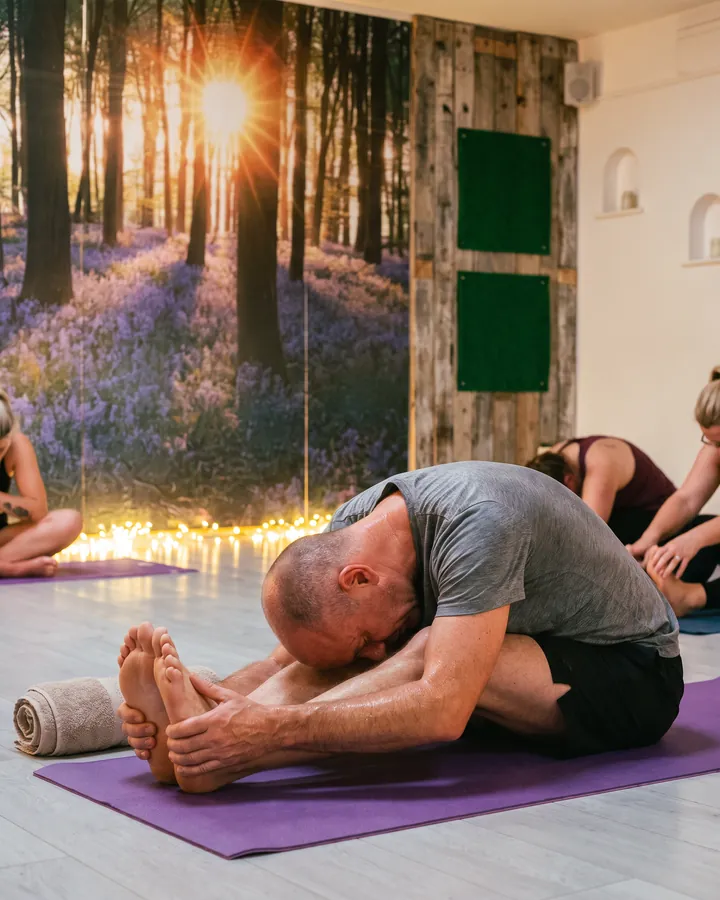 A man folding forward over his legs on a purple mat